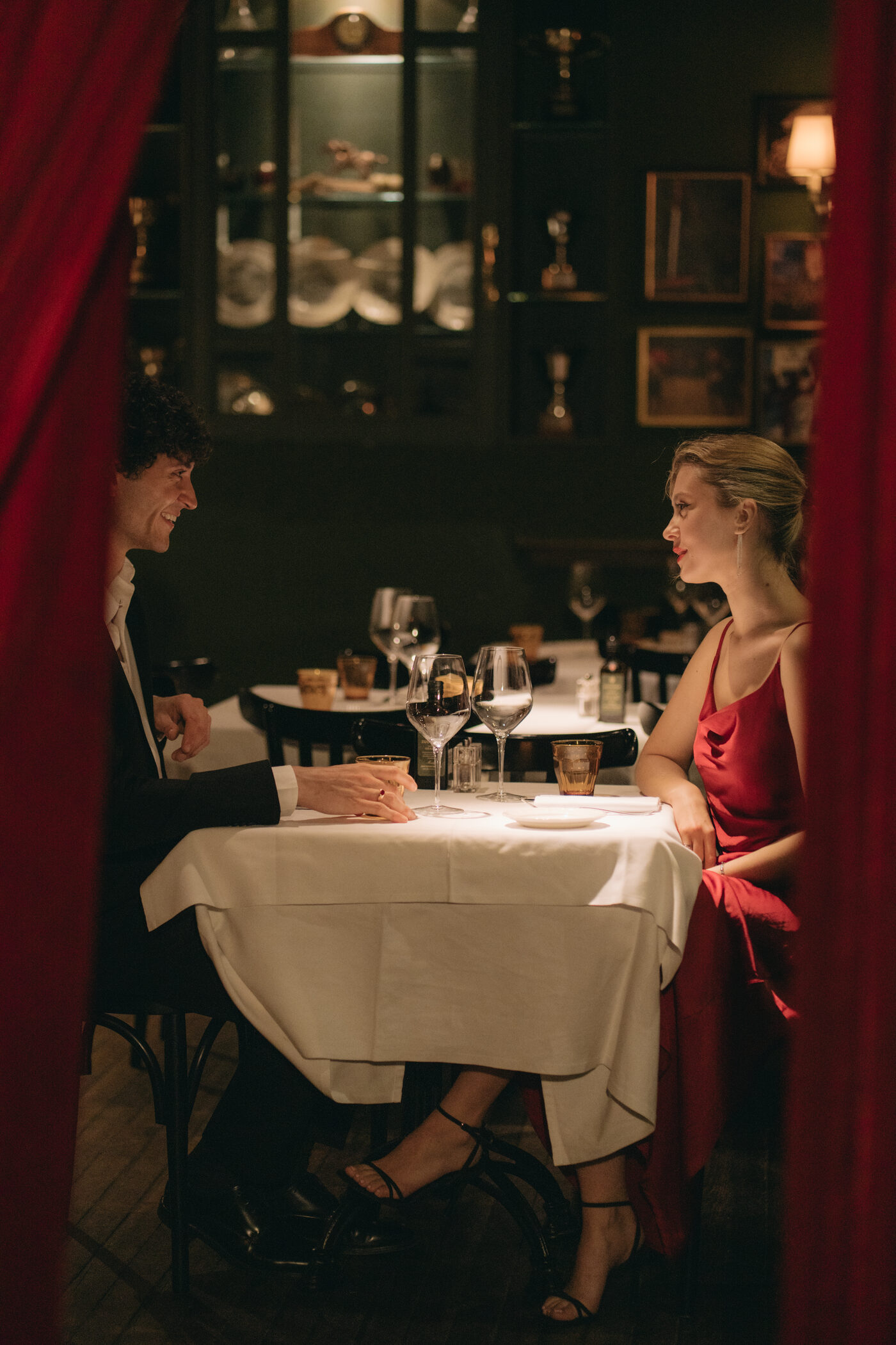 A couple at a candlelit table glimpsed through the red velvet curtain of the restaurant
