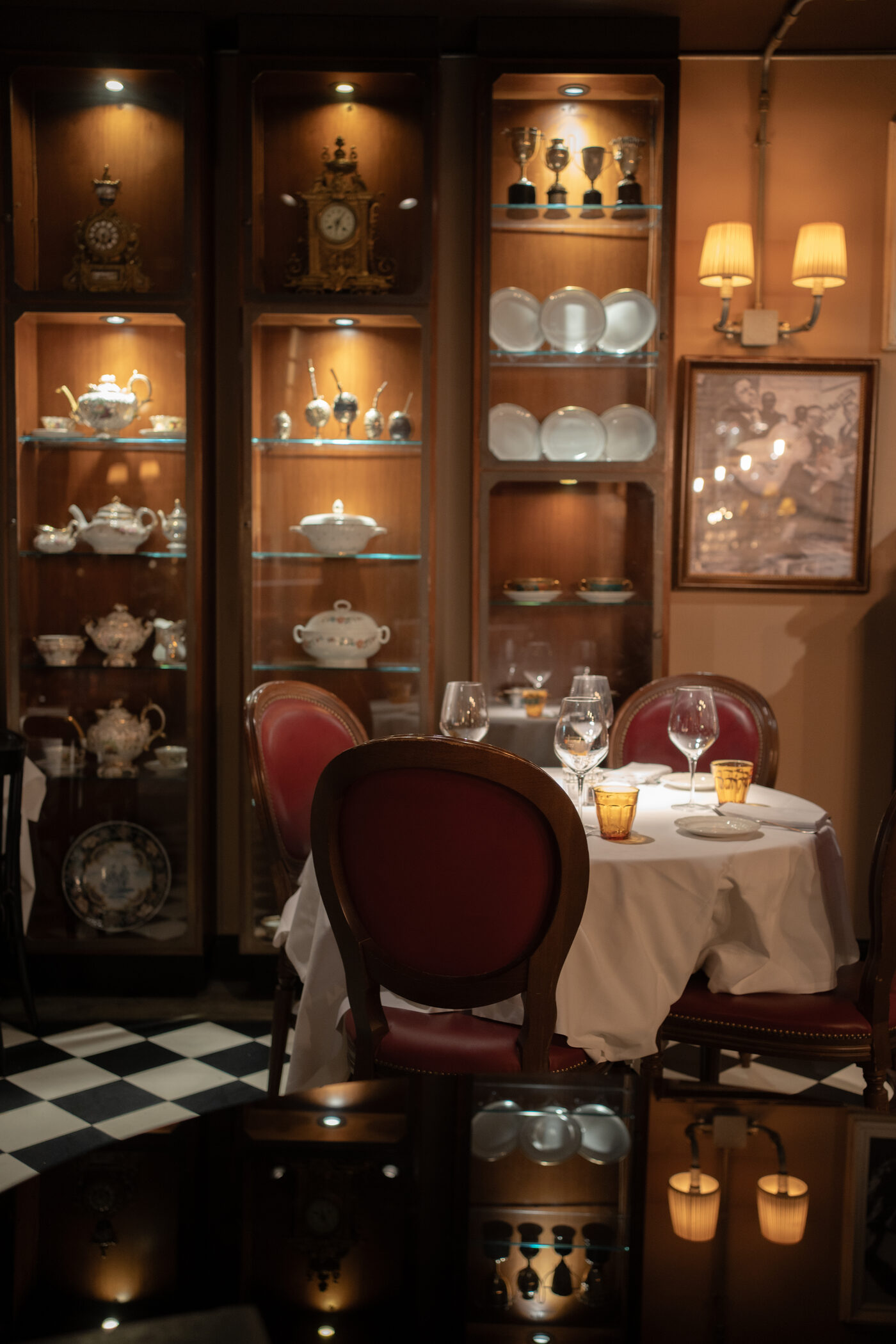 Illuminated cabinets of porcelain and silverware above a set table, checkered marble floor