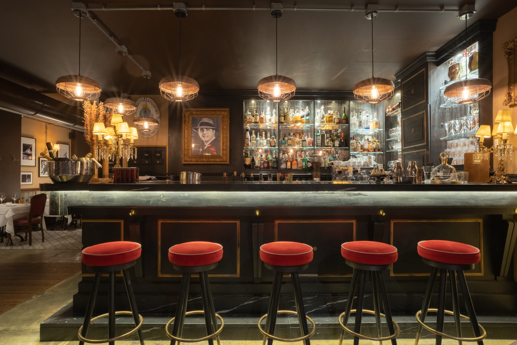 The bar of the restaurant at night — red velvet stools, brass and a wall of spirits