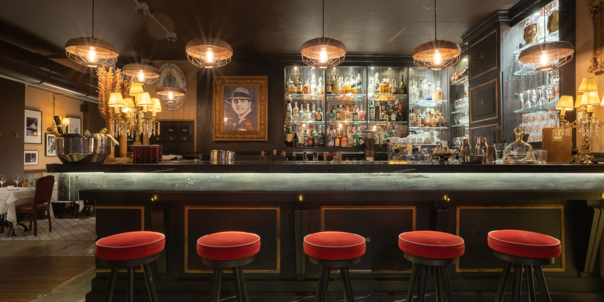 The bar of the restaurant at Speronari Suites by night — red velvet stools, brass and candlelight